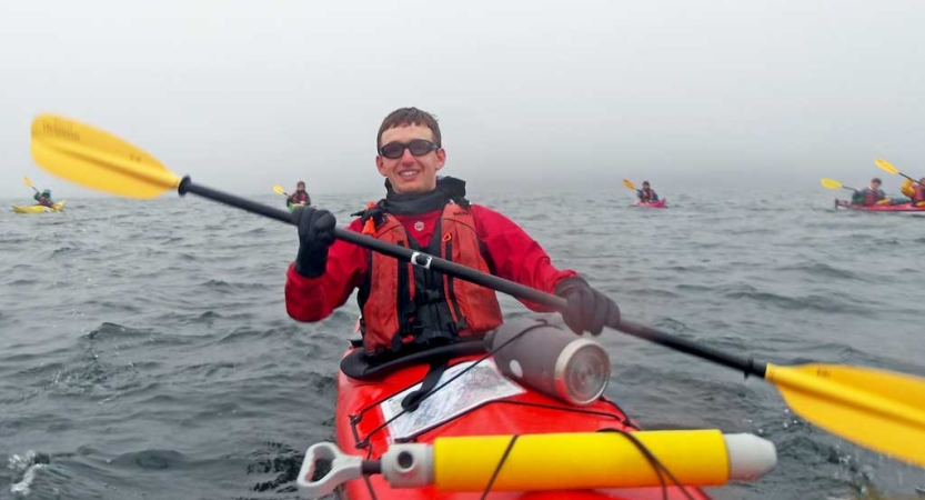 A person wearing a life jackets smiles while paddling a red kayak